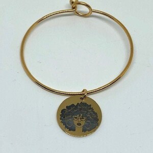 Puede incluir: Pulsera de oro con un dije que presenta una ilustración en blanco y negro de una mujer con un peinado afro y gafas.