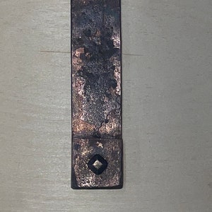Puede incluir: Un soporte de estante de metal r&uacute;stico con un dise&ntilde;o en forma de diamante en el centro. El soporte est&aacute; hecho de metal oscuro con un acabado desgastado.