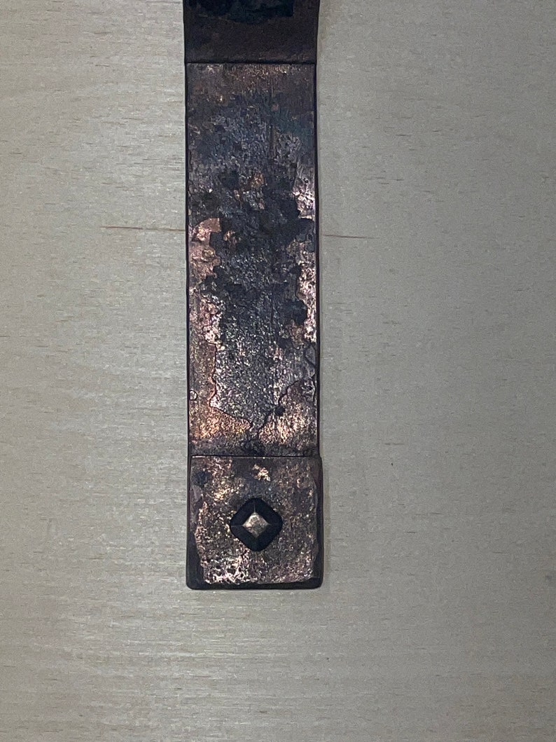Puede incluir: Un soporte de estante de metal r&uacute;stico con un dise&ntilde;o en forma de diamante en el centro. El soporte est&aacute; hecho de metal oscuro con un acabado desgastado.
