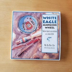 May include: A square book cover featuring a Native American theme. The cover displays a beaded plate with an eagle design, a flute, and feathers. Text on the cover reads "WHITE EAGLE MEDICINE WHEEL" and "Native American wisdom as a way of life."