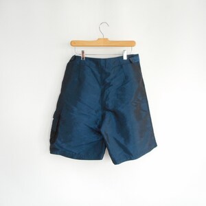 May include: Dark blue cargo shorts with a shiny finish. The shorts have a wide waistband and two pockets on the sides.