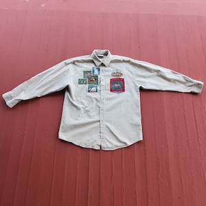 May include: A beige long-sleeve button-down shirt with multiple embroidered patches featuring animals and the text "Up North".