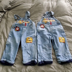 May include: Two pairs of blue and white striped overalls with a Mr. Fixit patch on each leg. The overalls have a yellow and red tool belt design on the front.