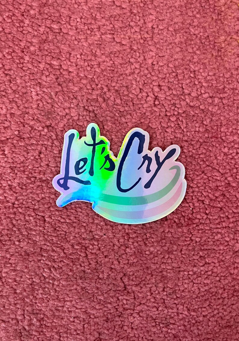 Peut inclure: Un autocollant holographique avec le texte "Let's Cry" en &eacute;criture noire. L'autocollant a une finition arc-en-ciel iris&eacute;e.