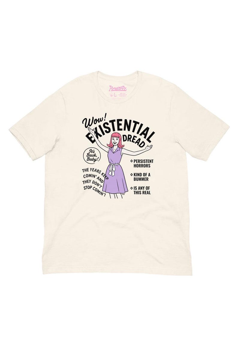 May include: Cream-colored t-shirt with the text "Wow! Existential Dread" and a cartoon illustration of a woman in a purple dress. Additional text includes "It's Back, Baby!" and "The years keep comin' and they don't stop comin'!"