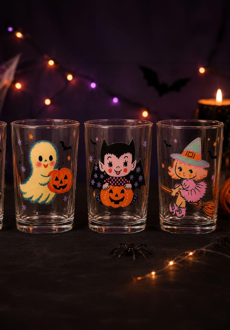 May include: Three clear glass tumblers featuring colorful Halloween-themed illustrations. The first glass shows a yellow ghost holding a pumpkin, the second a vampire with a pumpkin, and the third a witch on a broomstick with small stars and bats.