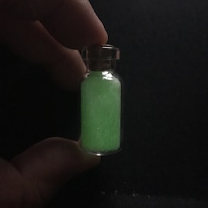 May include: A small glass bottle with a cork stopper filled with green glow-in-the-dark powder.
