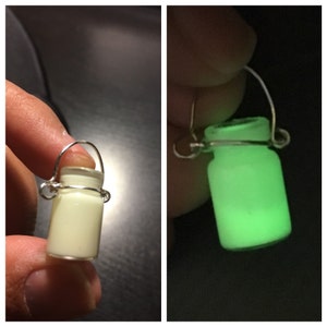 May include: A small glass jar with a metal handle, glowing green in the dark. The jar is a light green color when not glowing.