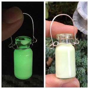 May include: A small glass milk bottle charm with a wire handle. The bottle is filled with a glowing green liquid. The bottle is shown in two images, one with the glow turned on and one with the glow turned off.
