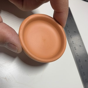 May include: A small, terracotta-colored, round planter with a smooth, slightly textured surface.