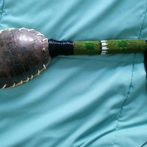 May include: A beaded turtle shell rattle with a green and black beaded handle and a long black tassel.