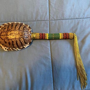 May include: A turtle shell rattle with a beaded handle and a long tassel. The handle is made with red, yellow, and green beads.