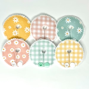May include: Six fabric circles with different patterns, including gingham and floral prints. Each circle has a hole in the center and a white button attached.