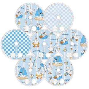 Puede incluir: Posavasos circulares con un tema de gansos caprichosos. Los posavasos presentan ilustraciones de gansos disfrutando de diversas actividades de verano, como navegar, pescar y nadar en flotadores. El fondo es azul claro con rayas blancas o un patrón de cuadros.