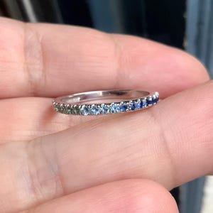 Könnte beinhalten: Ein Silberring mit einer Reihe von abgestuften blauen Saphiren. Die Saphire reichen von hellgrün bis tiefblau.