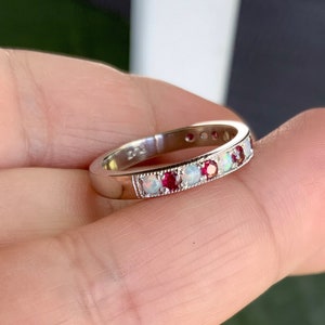 May include: A silver band ring with alternating red and white gemstones. The ring has a delicate, vintage-inspired design.