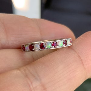 May include: A silver band ring with alternating red and white gemstones. The ring is set with small, round red rubies and white opals.