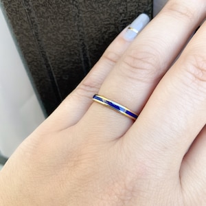 Puede incluir: Un anillo de oro con una banda fina, con una vibrante franja de esmalte azul. El anillo se muestra en una mano con u&ntilde;as cuidadas. El dise&ntilde;o del anillo es simple y elegante, adecuado para el uso diario u ocasiones especiales.