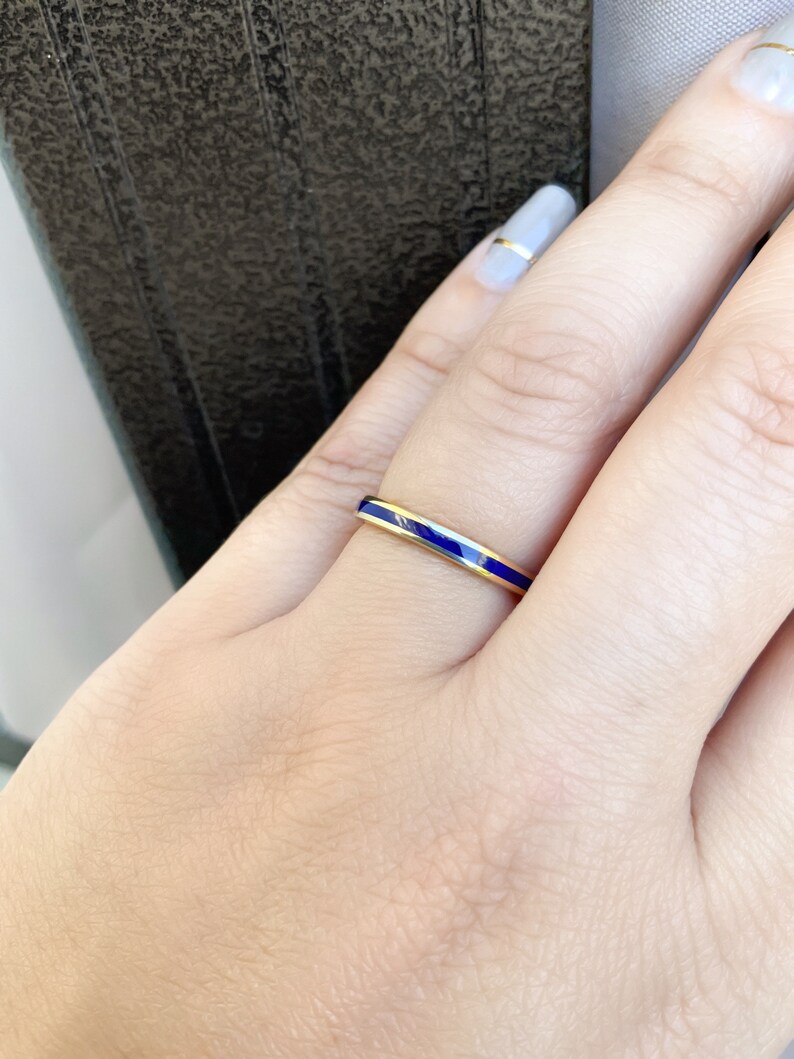 Puede incluir: Un anillo de oro con una banda fina, con una vibrante franja de esmalte azul. El anillo se muestra en una mano con u&ntilde;as cuidadas. El dise&ntilde;o del anillo es simple y elegante, adecuado para el uso diario u ocasiones especiales.