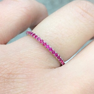 May include: A thin silver band with a row of small pink gemstones.