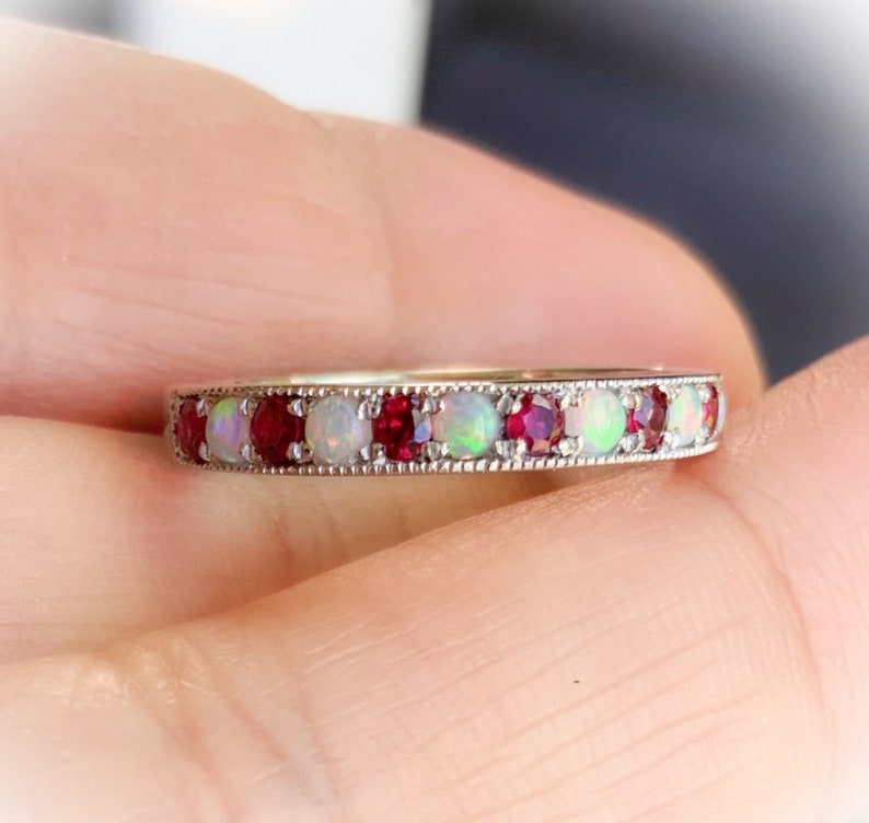 May include: A silver band ring with alternating red ruby and white opal gemstones.