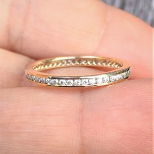 Könnte beinhalten: Ein dünner Goldring mit einer Reihe kleiner Diamanten, die in einer durchgehenden Linie um den gesamten Ring gelegt sind.