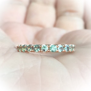 Könnte beinhalten: Ein zarter Goldring mit einer Reihe kleiner, runder, hellgrüner Edelsteine.