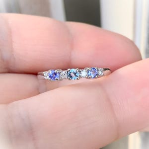 May include: A silver band ring with five gemstones. The centre stone is a larger, light blue gemstone. The other four stones are smaller, darker blue gemstones.