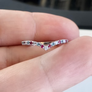 Könnte beinhalten: Ein zarter Silberring mit V-förmigem Design. Der Ring ist mit kleinen roten, blauen und weißen Edelsteinen verziert.