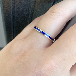 Puede incluir: Un anillo dorado con una banda delgada y una incrustaci&oacute;n de esmalte azul vibrante. El anillo presenta un dise&ntilde;o minimalista y elegante. El azul vibrante contrasta con el oro. Una joya sencilla y elegante.