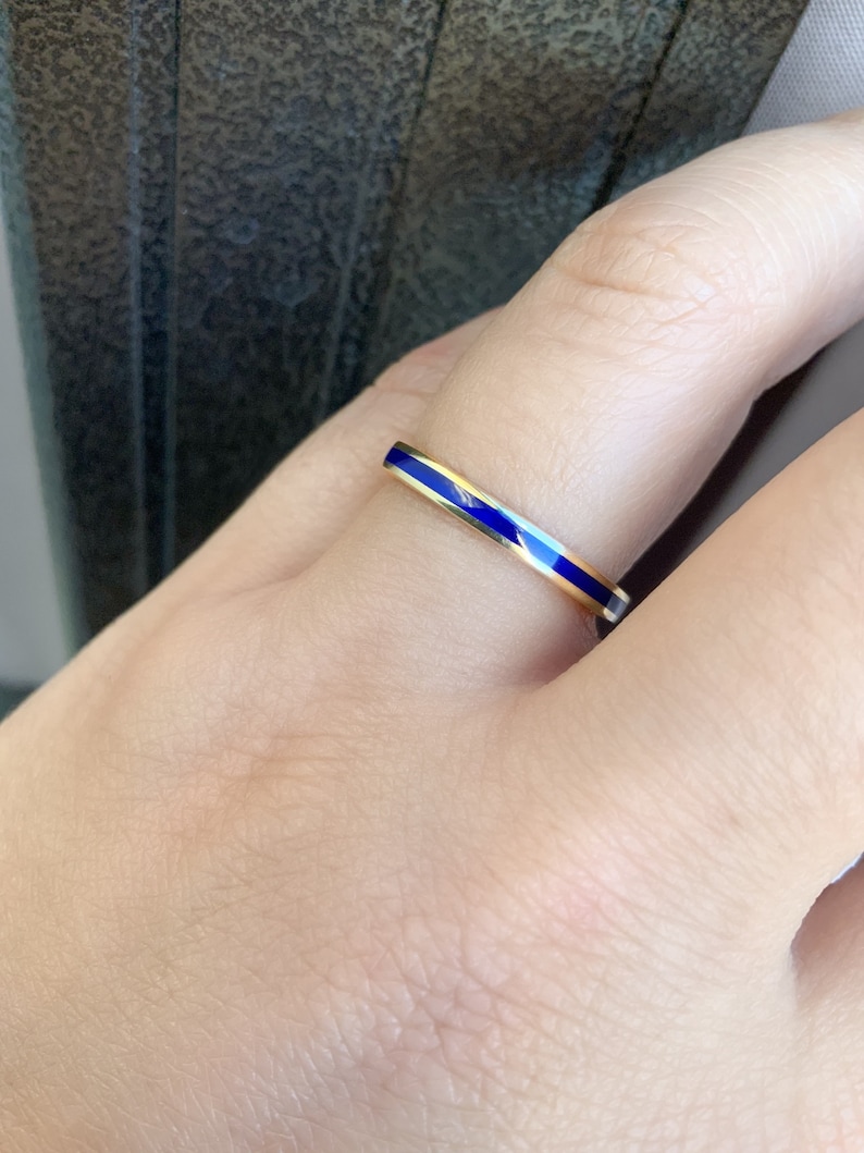 Puede incluir: Un anillo dorado con una banda delgada y una incrustaci&oacute;n de esmalte azul vibrante. El anillo presenta un dise&ntilde;o minimalista y elegante. El azul vibrante contrasta con el oro. Una joya sencilla y elegante.