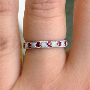 May include: A silver band ring with alternating red and white gemstones. The ring is set with small, round stones.