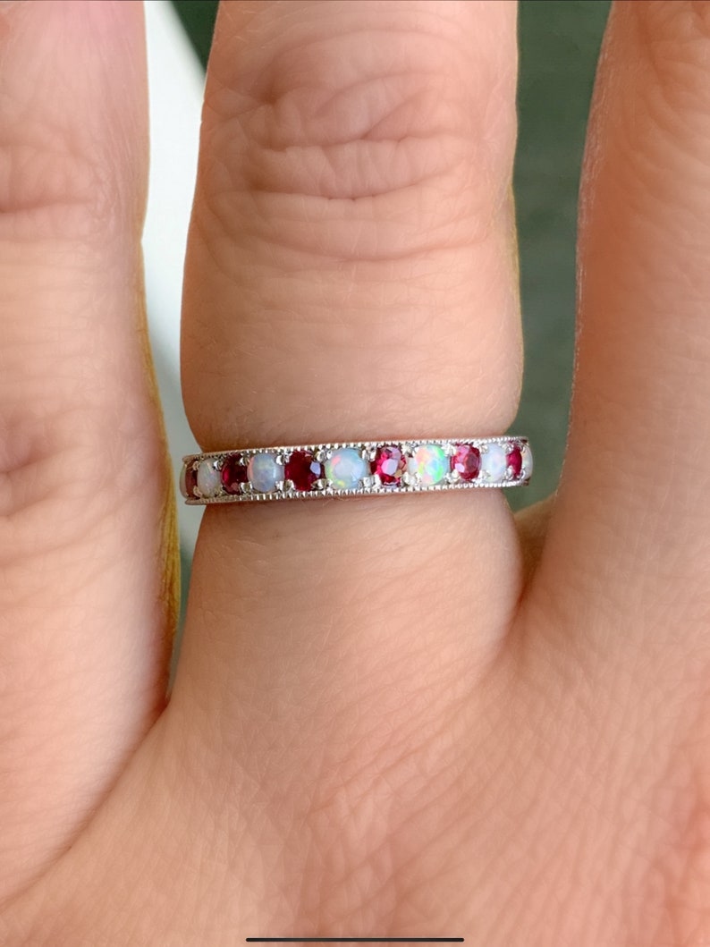 May include: A silver band ring with alternating red and white gemstones. The ring is set with small, round stones.