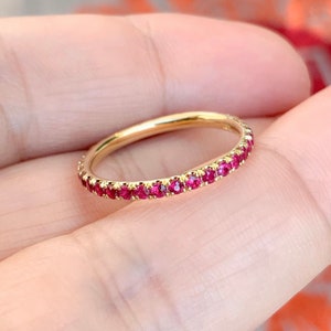 以下が含まれることがあります： 小さな鮮やかな赤い宝石が連続して並んだゴールドのバンドリング。 リングの宝石は互いにぴったりとセットされており、シームレスで輝く効果を生み出しています。 繊細なジュエリーです。