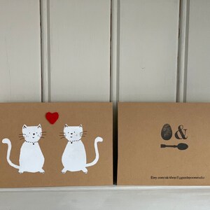 May include: Two brown cards with white cat illustrations and a red heart. The front card features two cats with collars and a heart. The back card has an egg and spoon design with the Etsy shop URL.