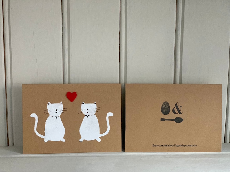 May include: Two brown cards with white cat illustrations and a red heart. The front card features two cats with collars and a heart. The back card has an egg and spoon design with the Etsy shop URL.