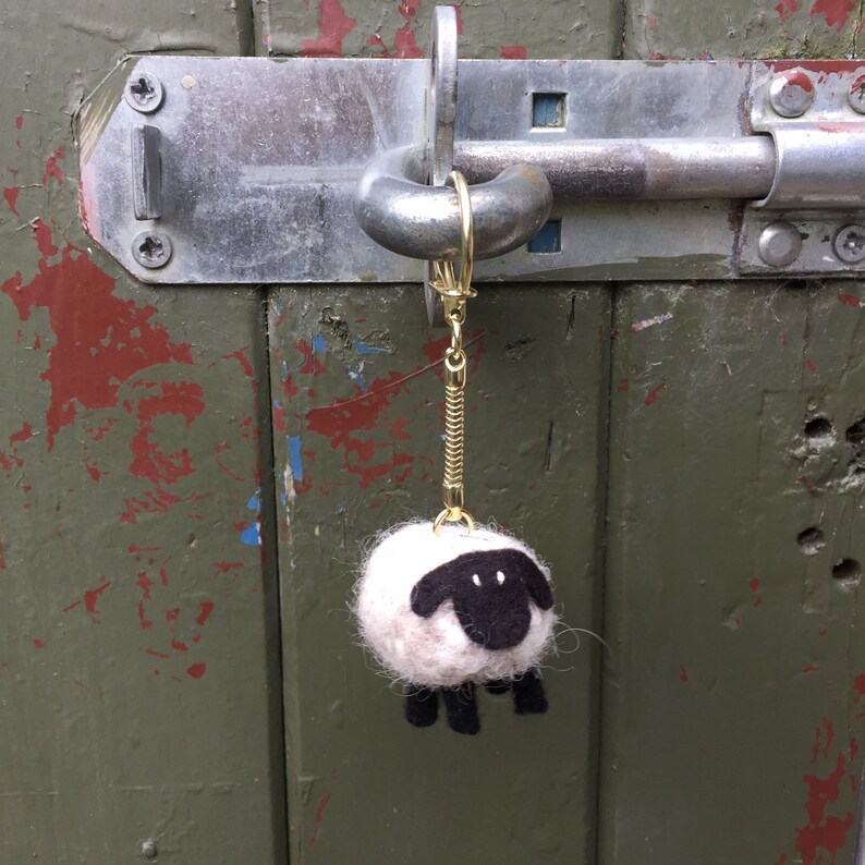 May include: A white and black felt sheep keychain hanging on a gold chain attached to a metal door latch.