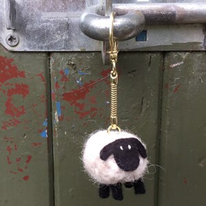 May include: A white and black felt sheep keychain with a gold chain attached to a metal ring.