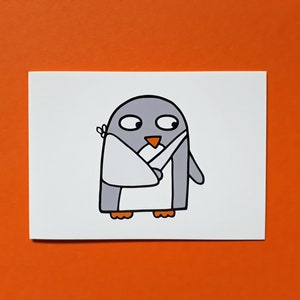 May include: A cartoon illustration of a penguin with grey and white colouring, an orange beak and feet, and a white bandage on its wing. The penguin is on a white rectangular card against an orange background.