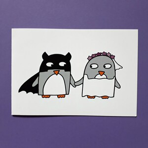 May include: A quirky illustration of two penguins holding hands. One is dressed as a bat, the other as a bride, wearing a veil and flower crown. The artwork is on a white background with a purple backdrop.