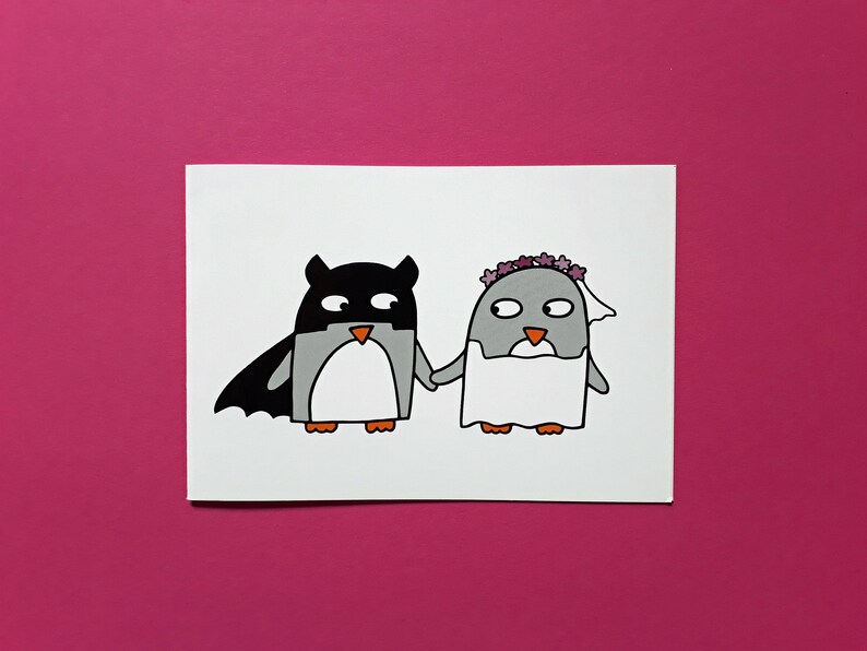May include: A charming illustration featuring two penguins. One is dressed as a superhero with a black mask and cape, the other as a bride with a floral crown and veil. They are holding hands. Set against a bright pink background.