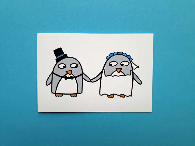 May include: A whimsical wedding card featuring two cartoon penguins holding hands. The penguin on the left wears a black top hat and bow tie, while the penguin on the right wears a veil and a blue floral headpiece. The card is set against a blue background.