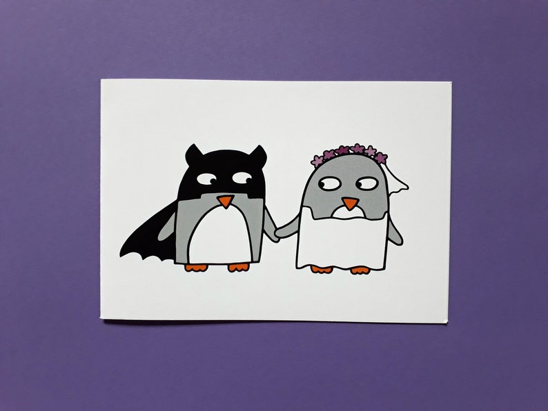May include: A charming illustration of two penguins holding hands. One is dressed as a superhero with a black mask and cape, the other as a bride with a veil and floral crown. The penguins are grey, black, and orange.