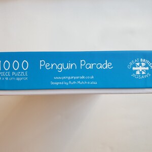 以下が含まれることがあります： 「1000 Piece Puzzle」と「Penguin Parade」の文字が入った青と白のパズルボックス。パズルのサイズは約69 x 48 cmです。ボックスには「Great British Jigsaws」の文字も含まれています。