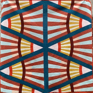 May include: A geometric quilt with a repeating pattern of red, blue, white, and yellow triangles and stripes. The quilt is made with a variety of fabrics and has a modern, abstract design.