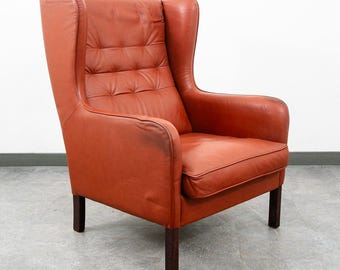 Poltrona de estilo dinamarquês moderno de meados do século XX, com encosto alto e abas laterais, em couro vermelho e capitonê.