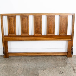 May include: A wooden headboard with a rectangular design. The headboard is made of light brown wood with a darker wood grain pattern on the rectangular panels. The headboard has a horizontal base and vertical supports, with metal hardware on the sides.