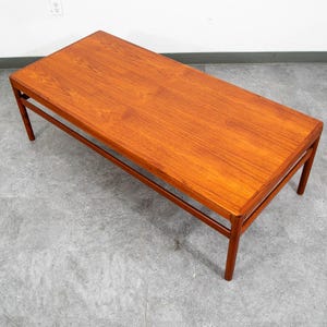 May include: A rectangular coffee table crafted from warm-toned wood with a smooth, polished surface. The table features four straight, tapered legs and a simple frame construction, showcasing a clear wood grain pattern across the top surface.