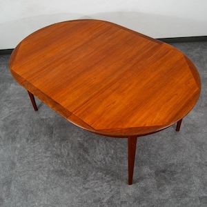 May include: A mid-century modern oval dining table with a rich, warm wood grain finish. The table has a unique, geometric edge design and four tapered legs. This piece of furniture is perfect for a dining room or kitchen.