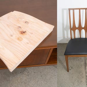 May include: A light-colored, curved wooden tabletop sits atop a dark brown cabinet. To the right, a wooden chair with a black seat and a decorative back is visible. The chair has four legs.